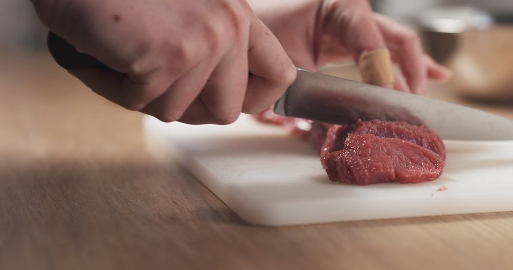 Cutting beef on chopping board in kitchen