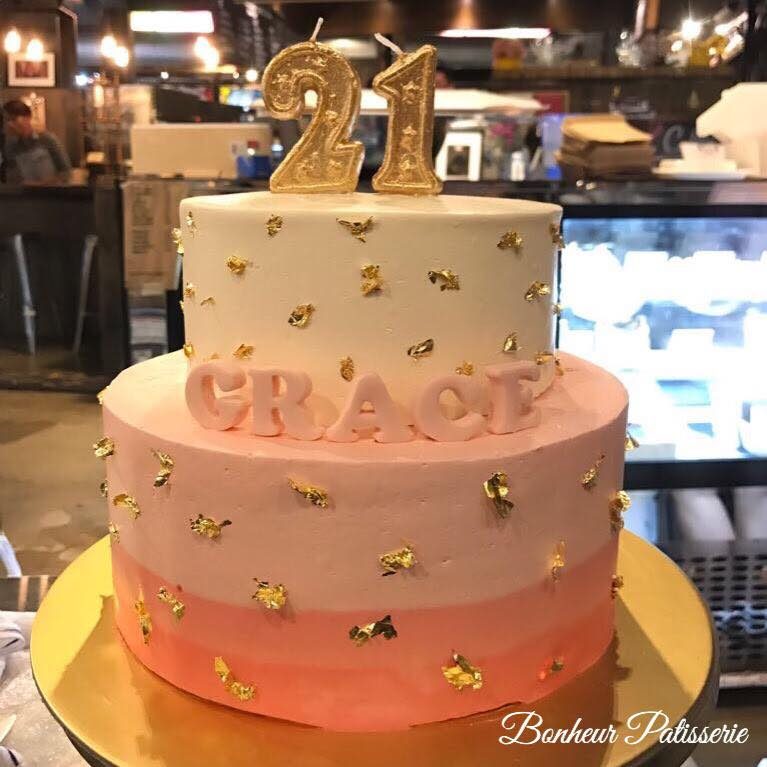 A sweet two-tiered birthday cake with pink ombre frosting with gold flakes and gold 21 candle on top. Made by: Bonheur Patisserie Singapore - Recommend.sg