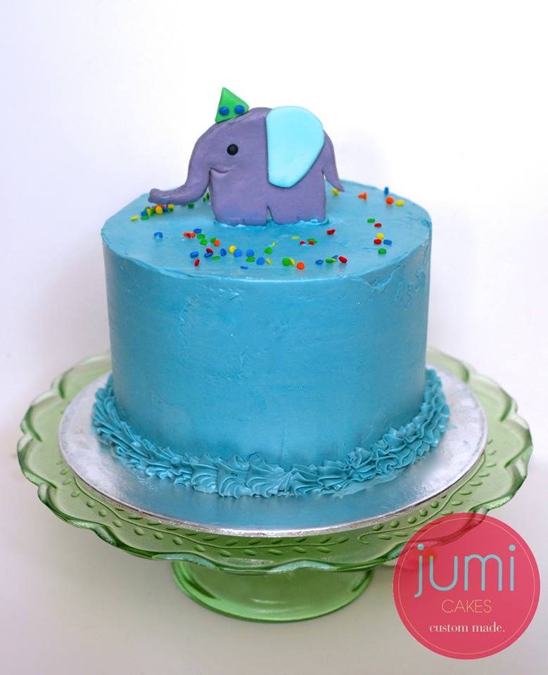 A tall round cake with blue cream cheese frosting with an elephant topper. Made by: Jumi Cakes Singapore - Recommend.sg