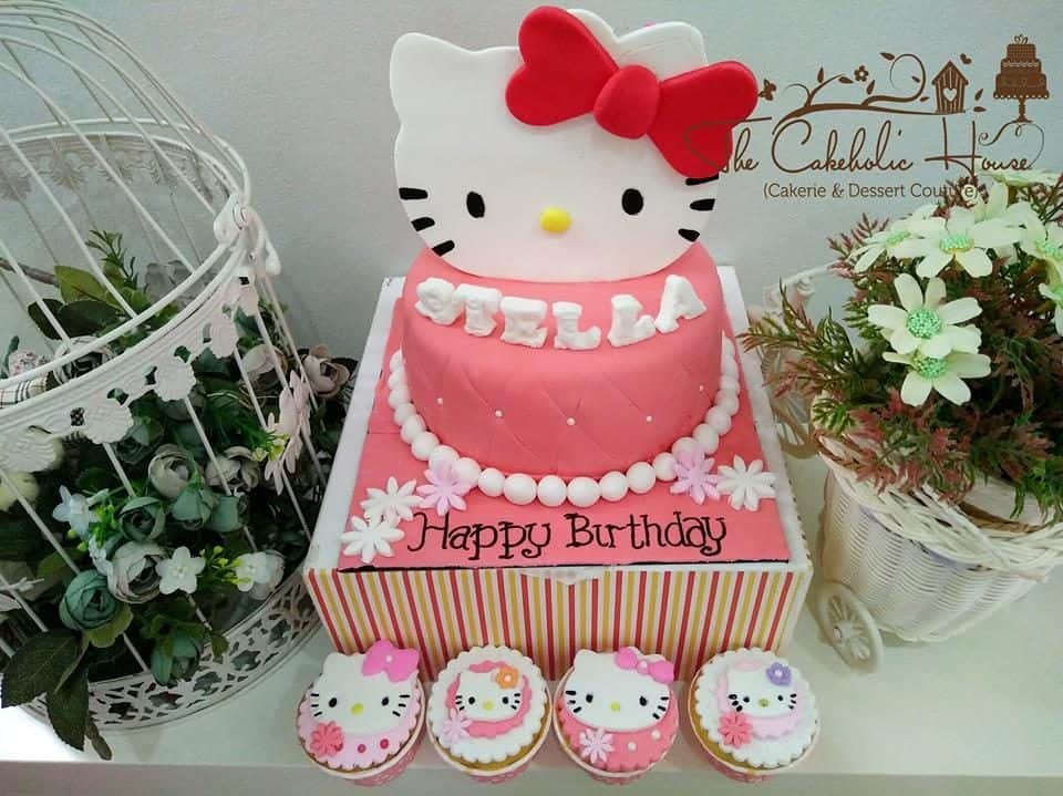 Cute cupcakes and a big round pink cake decorated with swiss dots, huge 2D Hello Kitty, and pearl candies sat on raised cake stand. Made by: The CakeHolic House. Source 