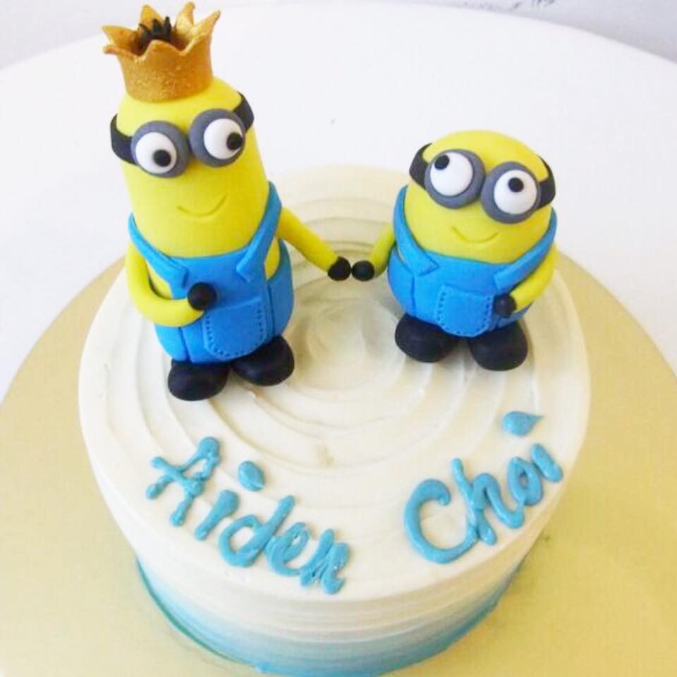 A round cake with blue ombre buttercream frosting, topped with two edible Minion figurines.Made by: Corine and Cake.Source
