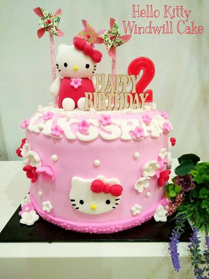 Hello Kitty with windmill toppers on top of a round, single tiered cake decorated with Hello Kitty and flower cutouts.Made by: The CakeHolic House. Source