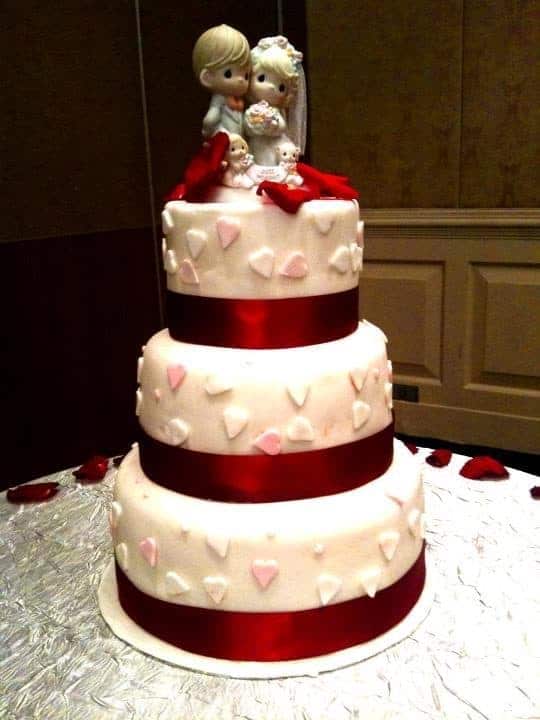 The cake artist keeps the three-tiered white cake simple with heart shaped cutouts and red ribbons. Made by: My Fat Lady Cakes and Bakes.Source