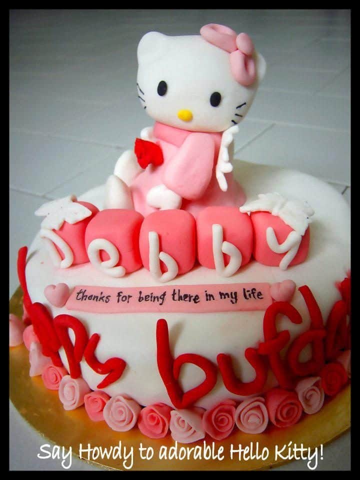 A small sized, round cake with, again, fondant icing is surrounded by small flower, and alphabet shaped fondant sculpted by hand, and a big angel Hello Kitty on top.. Made by: Leenie's Bakery.Source