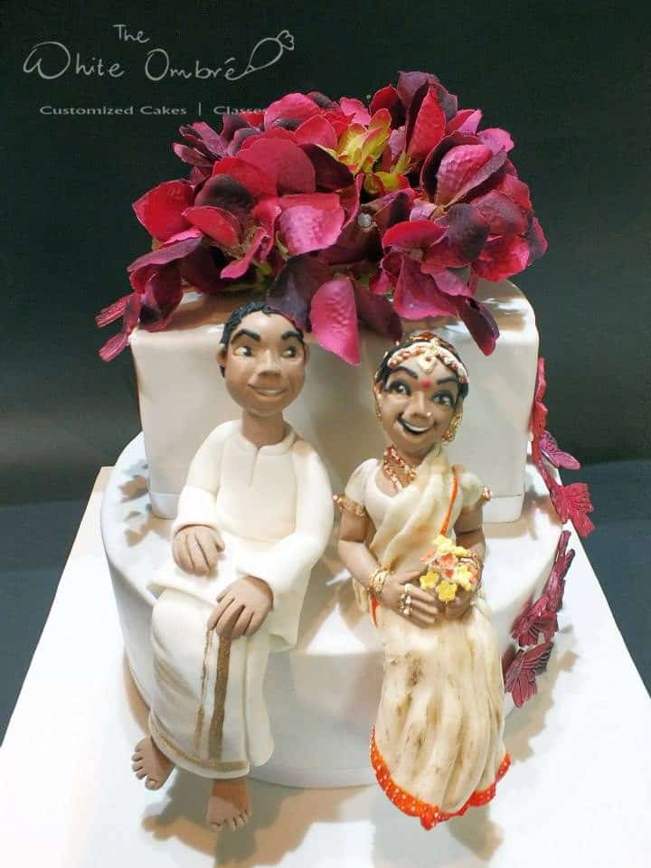 A two-tiered cake with figurines of the bride and groom in Indian traditional attire is perfect for a traditional Indian wedding.Made by: The White Ombre.Source