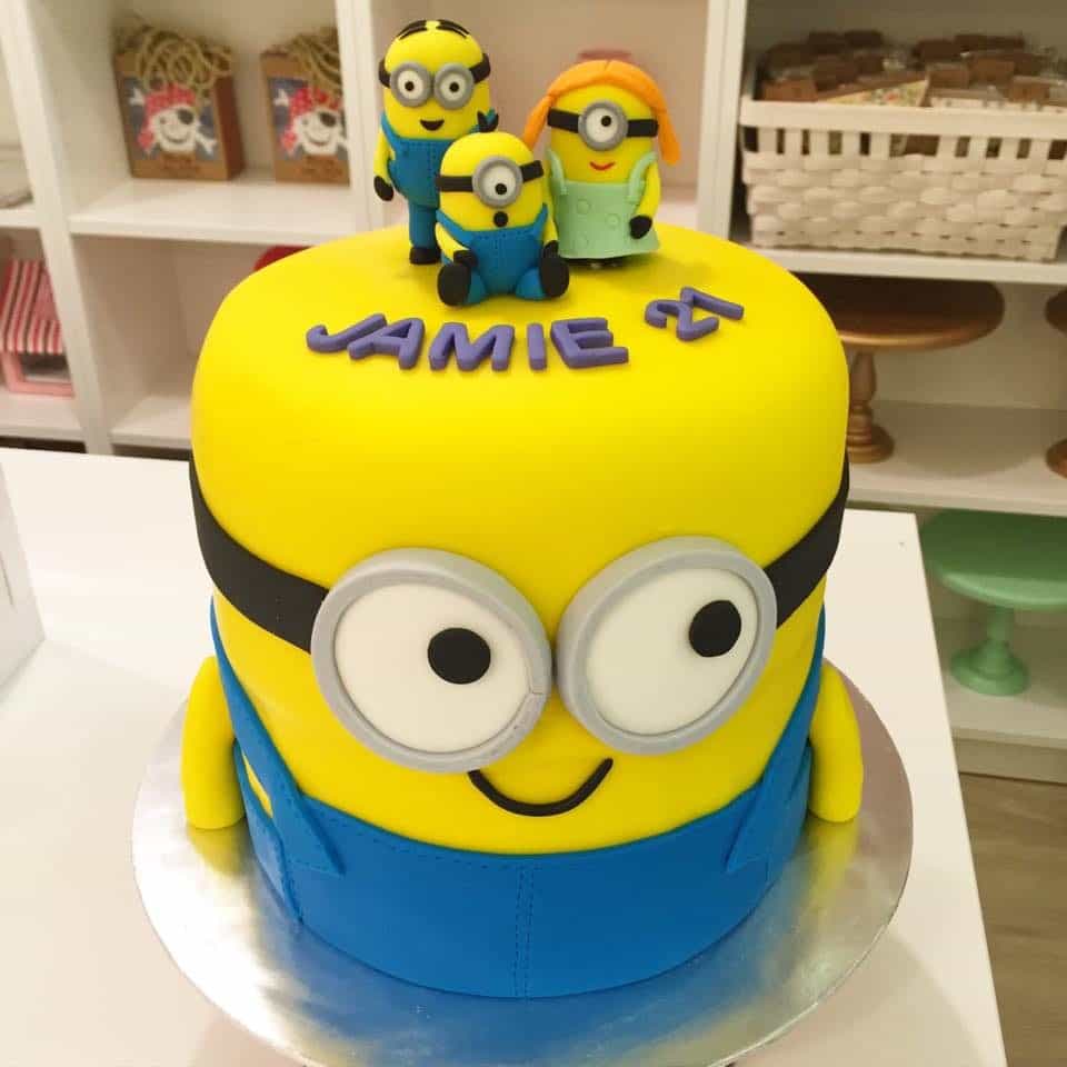 A tall round Minion shaped cake with three little Minion figurines as the cake topper.Made by: Little House of Dreams.Source